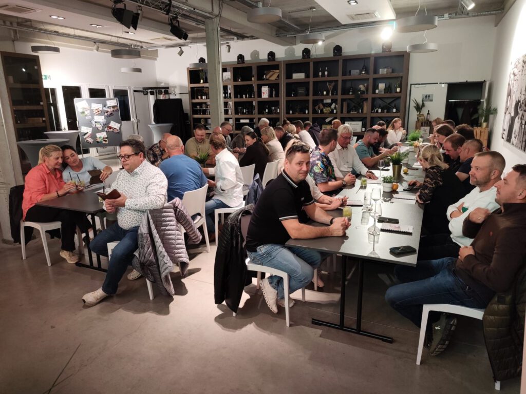 Gäste an langen Tischen vor den Weinregalen der Eventlocation
