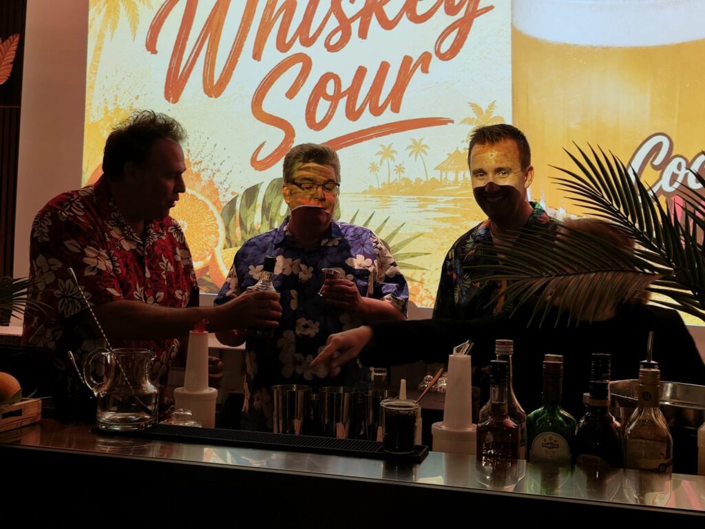 Der Vorstand in Hawaiihemden mixt Whiskey Sour an der Cocktailbar